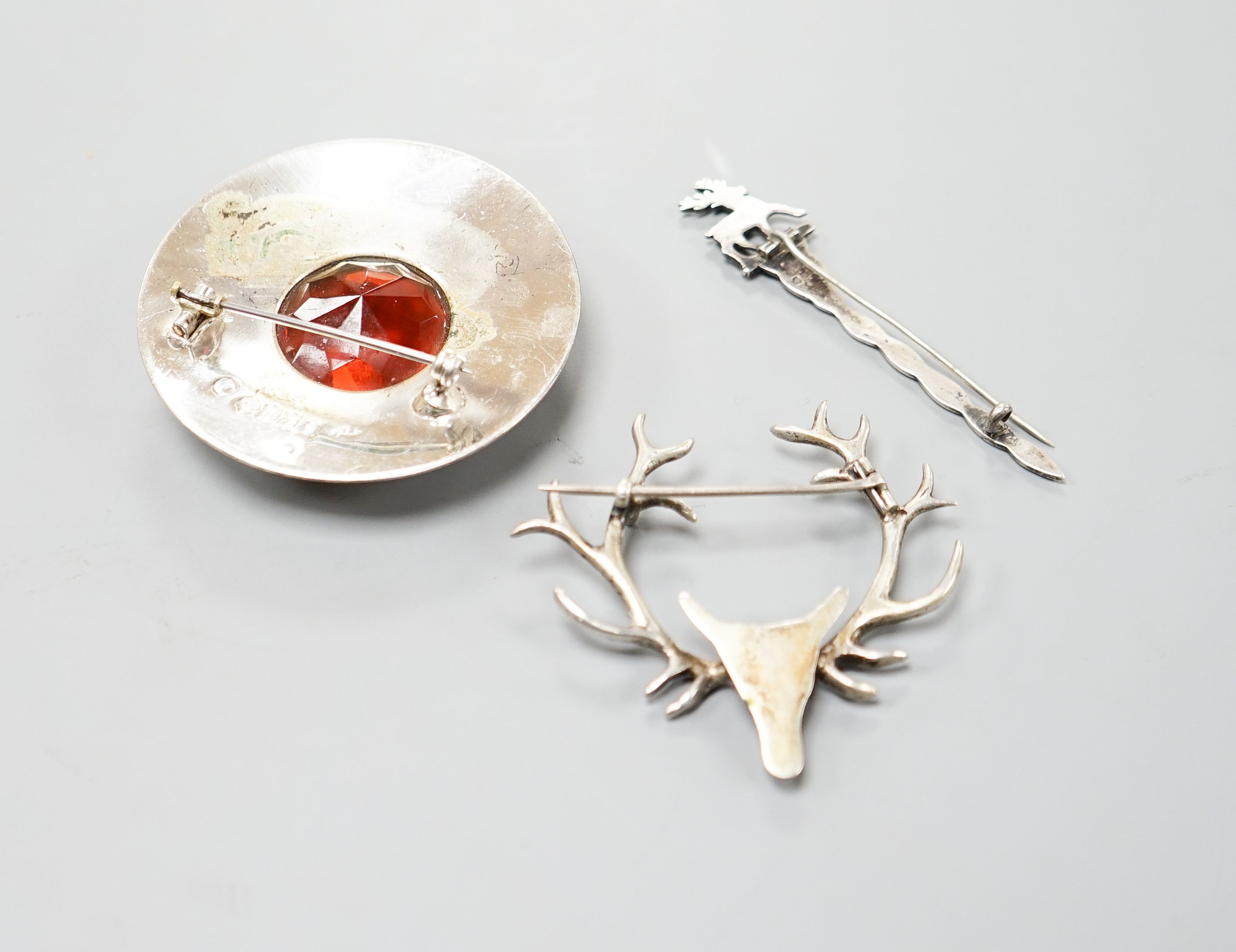 A Scottish silver and paste set circular brooch, Glasgow, 1952, together with a Scottish silver brooch, with stag terminal and one other metal stag head brooch.